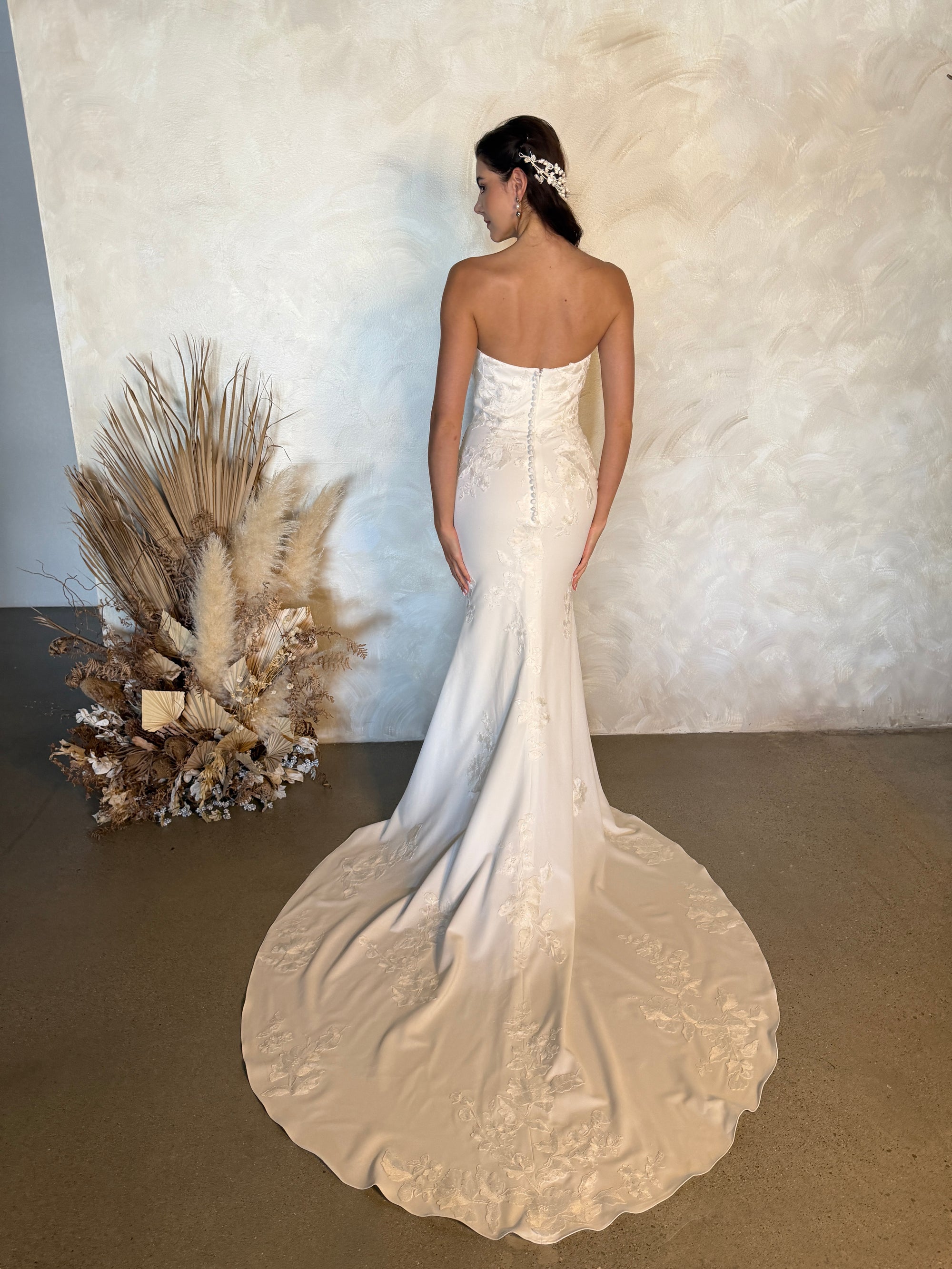 Back view of the Aveline fitted strapless wedding dress with covered buttons and a floral appliqué train