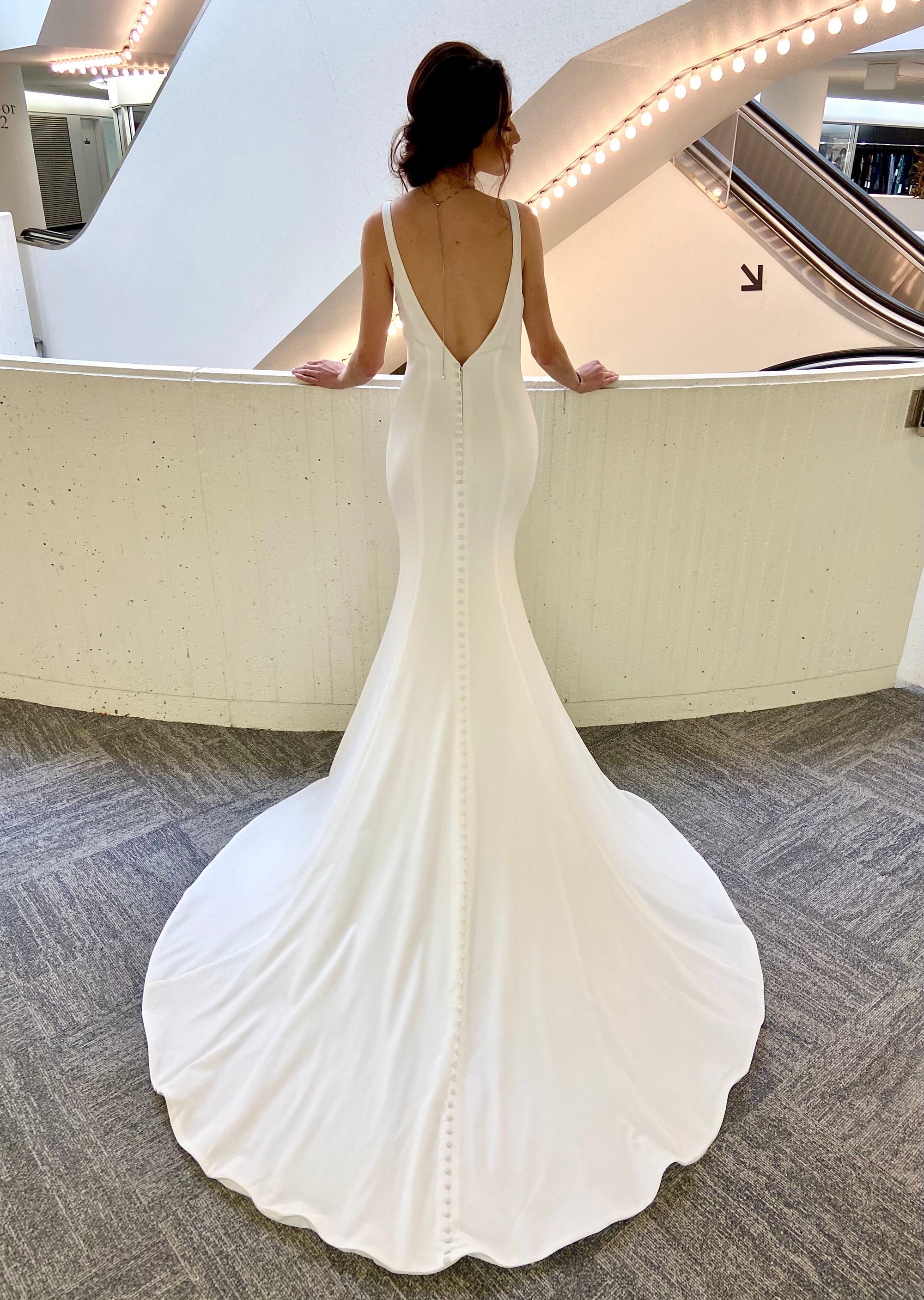 Back view of the Bliss Gown featuring a low V-back, covered buttons and a long sweeping wedding dress train.