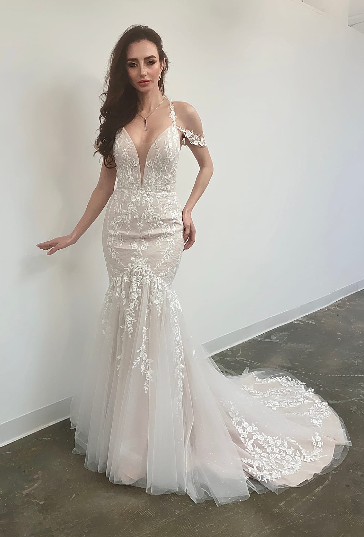 Front view of the Elowen Gown, an off-shoulder lace fit-and-flare wedding dress with a plunging V-neckline and floral appliqué.