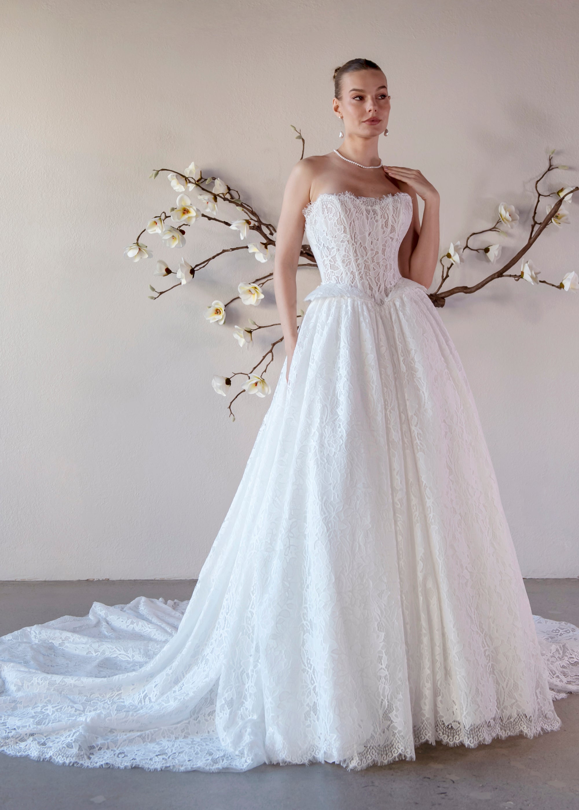 Three-quarter front view of the Isolde strapless lace ball gown with a basque waist, sculptural hip details, and flowing train