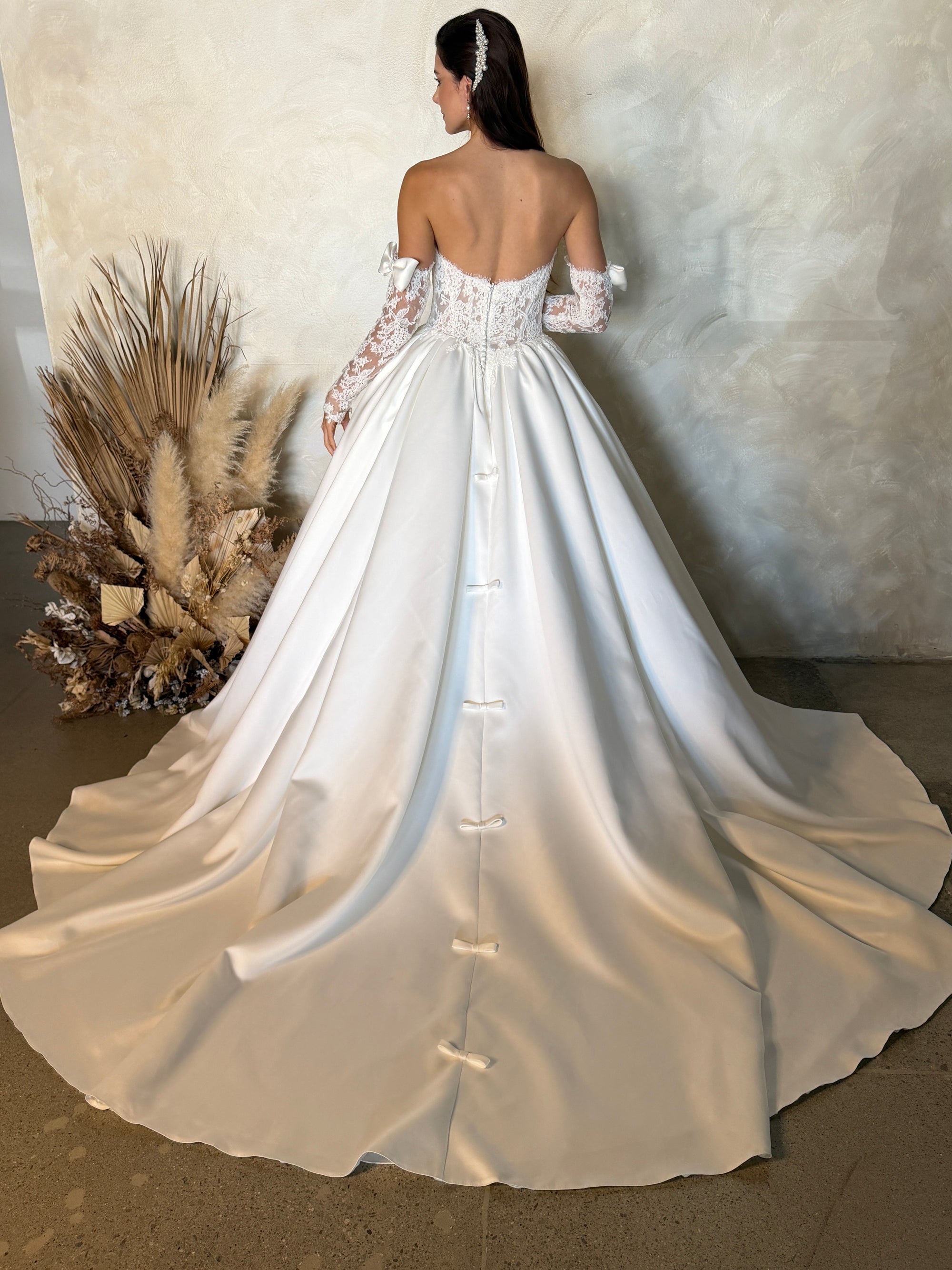 Back view of the Marcelline French lace ball gown without the detachable bow, showing the corset bodice and pleated train
