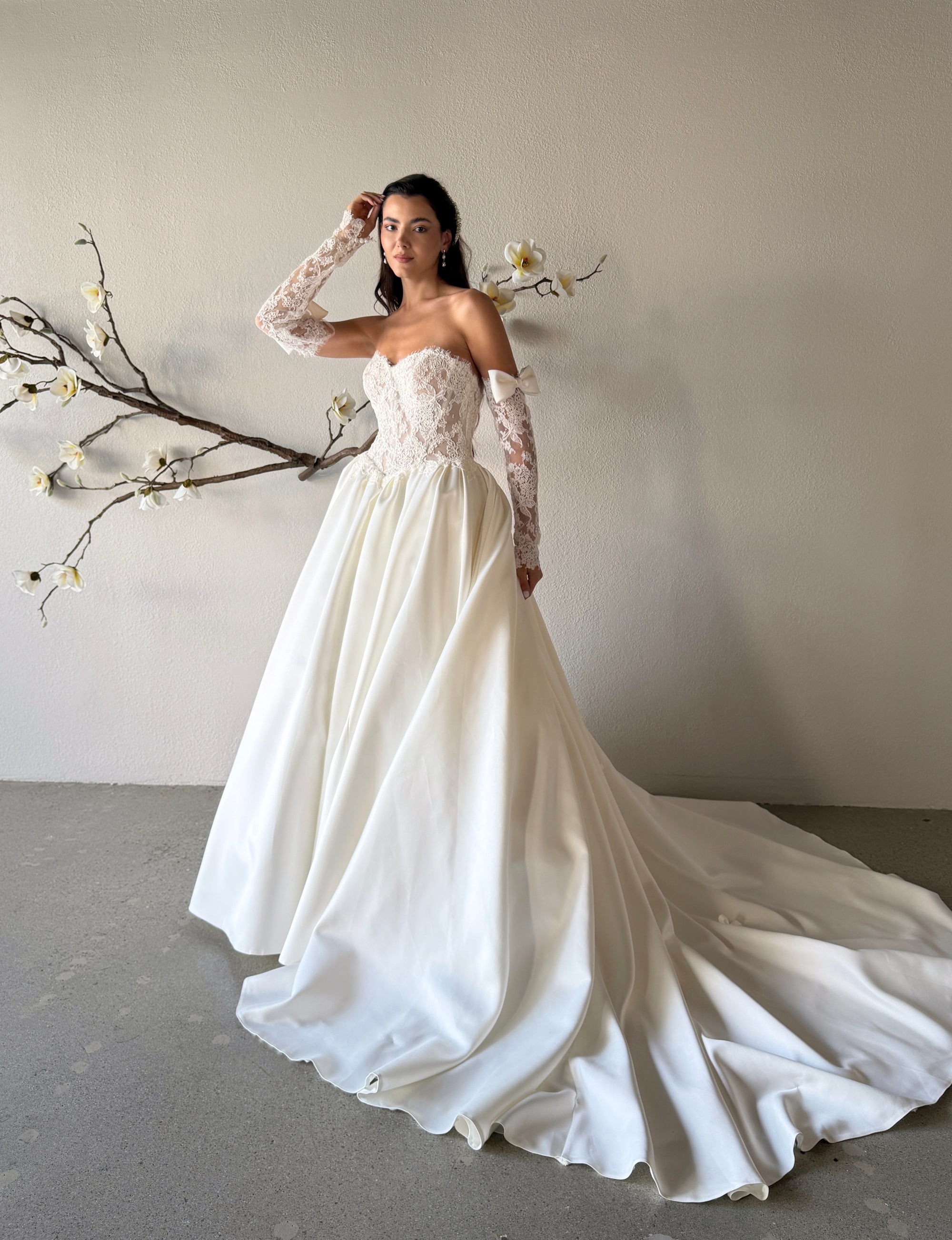 Three-quarter front view of the Marcelline French lace ball gown with a basque waist, detachable sleeves, and structured pleated skirt