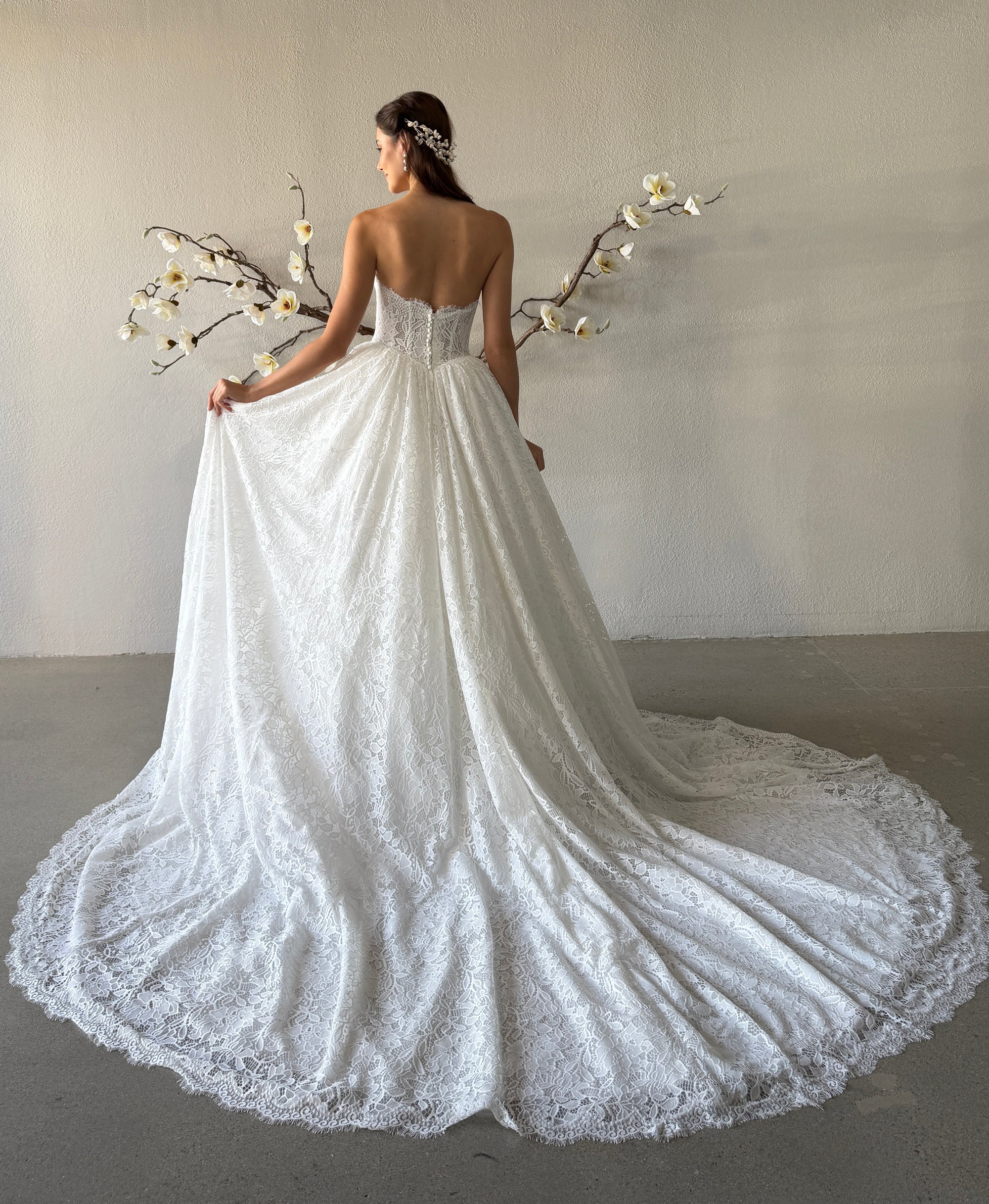 Back view of the Seraphine lace ball gown with a low scoop back, covered buttons, and detachable overskirt with an elegant train