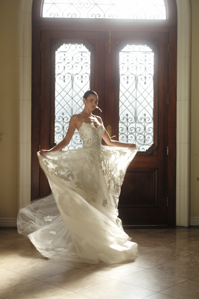 Three-quarter back view of the Sovereign organza ball gown featuring dimensional floral appliqué and a statement train